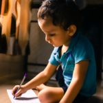 boy writing on white paper