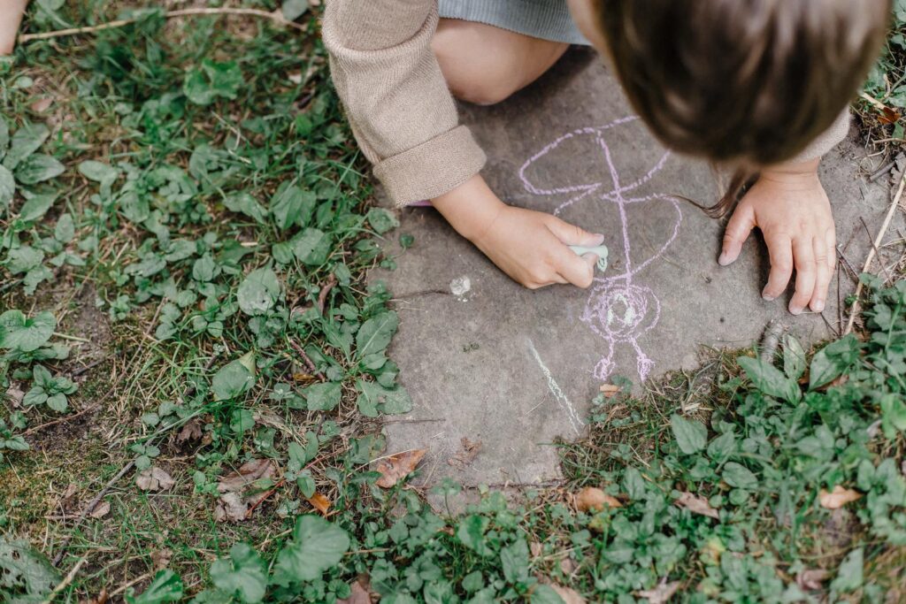 Faceless kid drawing on ground with chalk in green park