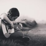 grayscaled photo of boy playing guitar