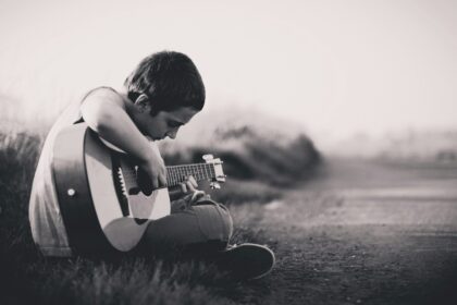 grayscaled photo of boy playing guitar