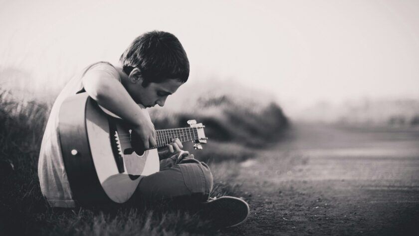 grayscaled photo of boy playing guitar